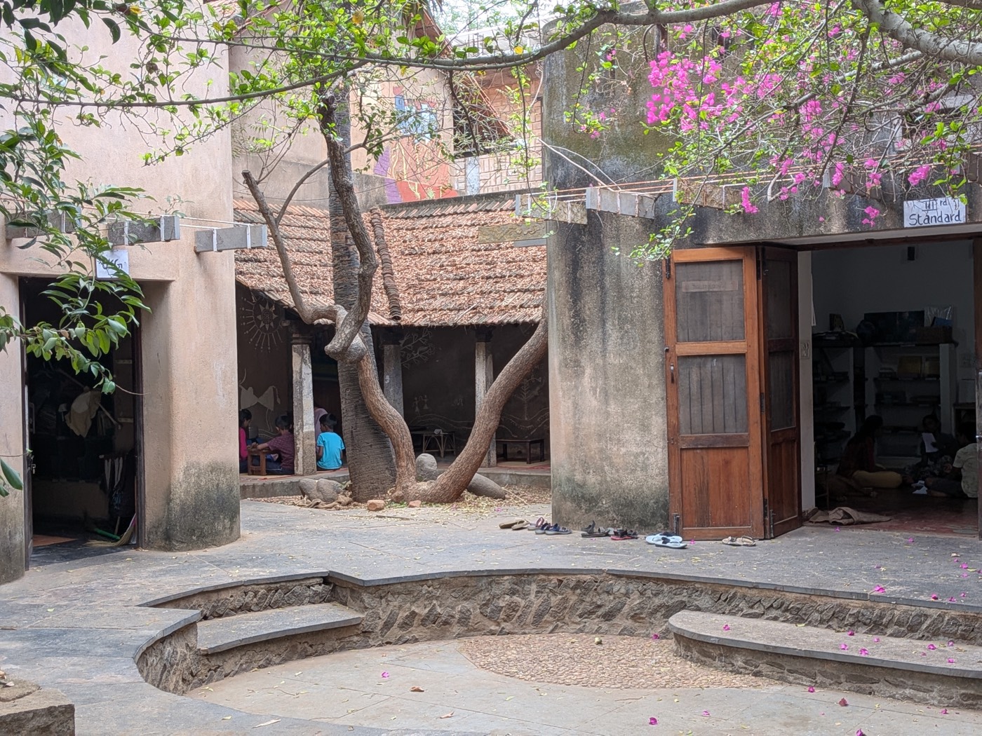 The courtyard of an alternative school in Tamil Nadu, a tree and flowering bougainvillea framing the open learning space.